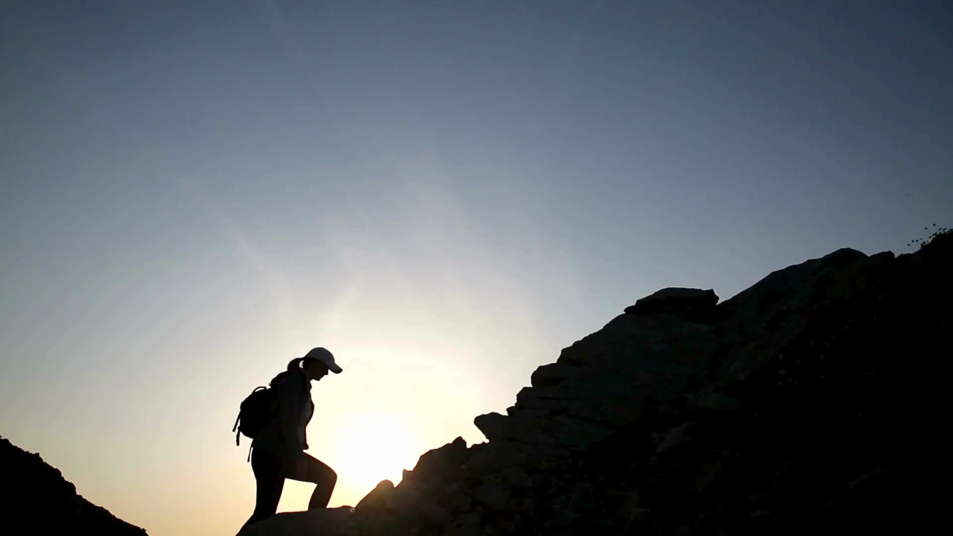Silhouette of a hiker climbing a rocky ridge at sunset
